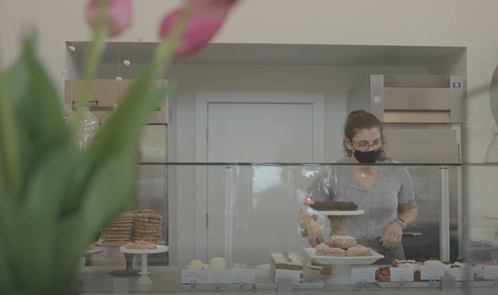 a woman in a kitchen preparing food behind a glass counter