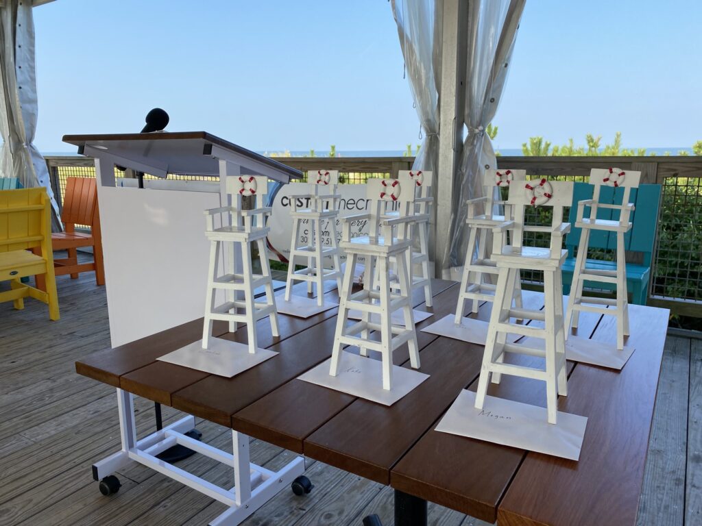 a wooden table topped with white chairs next to a window